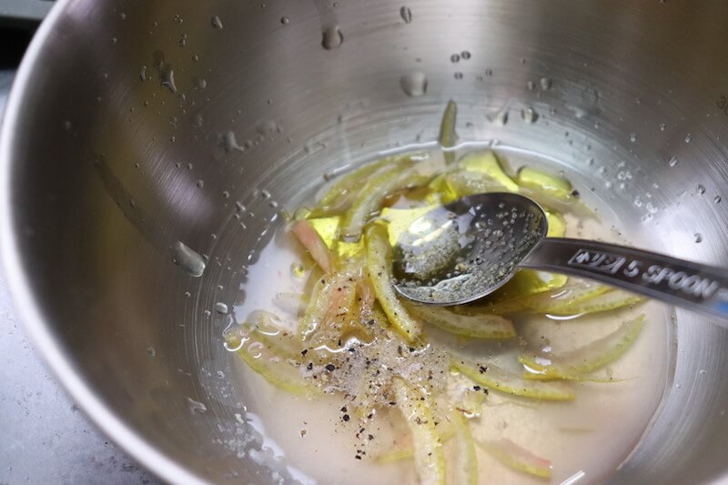 レモンの皮を千切りにしてボウルに入れて果汁を絞り、オリーブオイル・砂糖・こしょうを混ぜる
